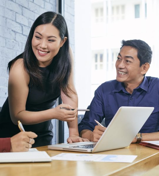 Smiling Vietnamese businesswoman discussing presentations on laptop screen with colleagues